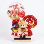 Ancheta romántica en caja de madera con peluche de oso coronado, rosas rojas en satín, chocolates y globo burbuja Te Amo sobre fondo blanco